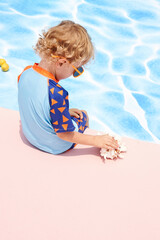 Child playing by the pool in colorful swimwear, enjoying the sunny day.