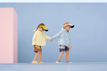 Two children playing outdoors in stylish colorful sun hats and hoodies.