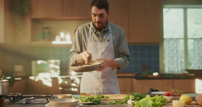 Professional Home Cook Preparing a Meal in a Modern Kitchen. Wearing an Apron, Caucasian Man Mixes Ingredients, Smells the Flavour, Making His Favorite Italian Pasta Recipe. Zoom Out Footage