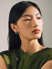 Elegant woman in a green top with subtle makeup and earrings, exuding modern beauty.