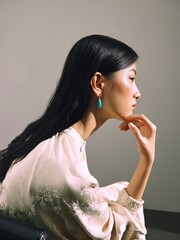 Profile shot of a woman wearing a light silk top and turquoise earrings, conveying elegance and modern beauty.