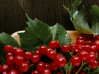 Red berries and green leaves in wooden bowl on dark wood, perfect for autumn and organic themes.