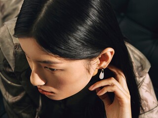 Woman in elegant attire with statement earrings adjusting her hair, conveying modern elegance and confidence.