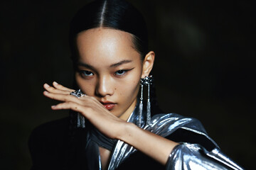 Portrait of a woman in a silver outfit with dramatic makeup and unique pose conveying modern elegance.