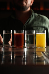 Man drinking at a bar, reaching for a lineup of four colorful shooters (clear, red, yellow). Close-up of a patron enjoying the nightlife and bar experience.