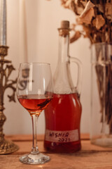Homemade cherry liqueur with candles and dried roses on a rustic wooden table