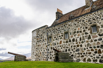 Duart Castle - Old stone castle with cannons on green grass under cloudy skies, showcasing historical military architecture and heritage charm.