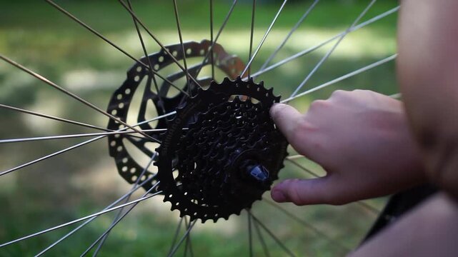 boys finger turning a bicycle cassette gear and rear wheel disc brake outdoors concept of bicycle repair, bike maintenance, active childhood