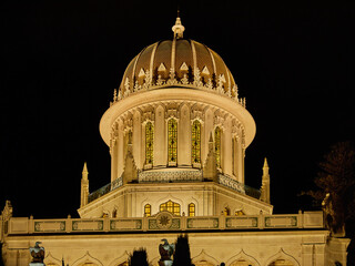 Zoomed view of Bahai Shrine dome at night, showcasing architectural details under warm illumination against a dark sky.