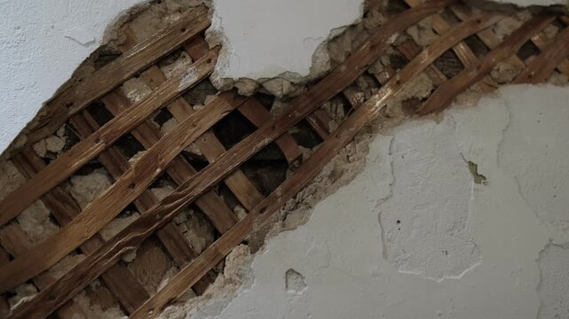 Old damaged wall with exposed wooden lath and cracked plaster texture construction detail