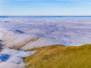 Mountain ridge emerging from a thick blanket of clouds with clear blue sky above