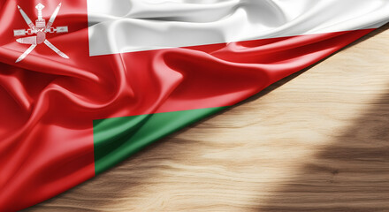 A close-up, detailed shot of the rich, satin fabric of the Omani flag draped over a wooden surface.