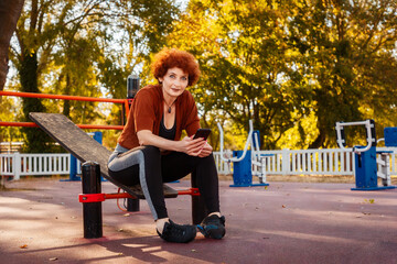 Mid adult Caucasian curly-haired woman sitting at sports ground and using cell phone. Concept of motivation and activity
