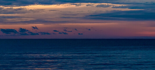 Obraz premium Wide expanse of deep blue ocean meeting a horizon under a dusk sky featuring layers of dark and pale orange clouds.