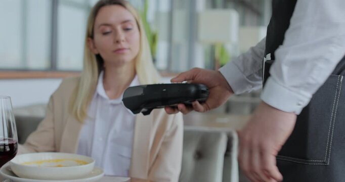 Woman paying restaurant bill using smartphone. Waiter giving terminal for cashless payment to woman. Technology device concept.