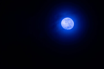 Bright full moon glowing in the dark night sky with deep blue aura, symbolizing mystery, beauty, and tranquility. Perfect background for nature, astronomy, and night-themed concepts.