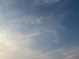 Soft blue sky with gentle wispy clouds illuminated by warm sunlight above a faint horizon. A tranquil and dreamy atmosphere ideal for nature, background, or weather-themed visuals.