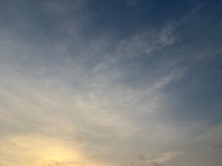 Soft blue sky with gentle wispy clouds illuminated by warm sunlight above a faint horizon. A tranquil and dreamy atmosphere ideal for nature, background, or weather-themed visuals.