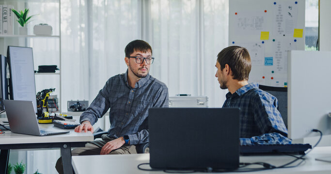 Adult male engineer team discusses AI software development robotic hand project use AI code solutions at tech workspace. Artificial intelligence interface, collaboration support prototype development.