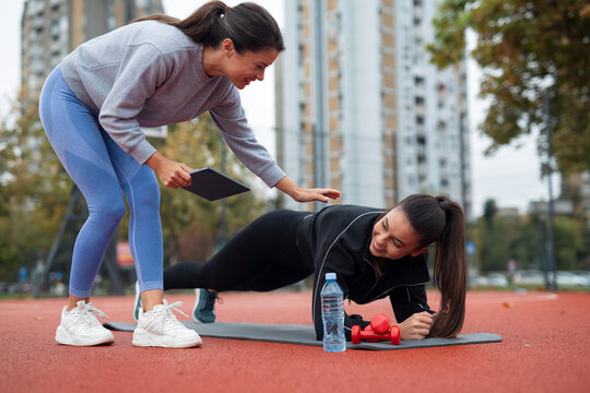Personal trainer assisting woman doing plank exercise outdoor