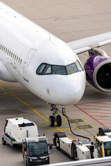 Modern regional  jet aircraft airport tarmac connected to ground vehicles for refueling maintenance. Engine cockpit clearly visible crew performs technical operations before next scheduled flight