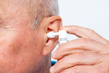 Close up mature senior man ear treatment with medical spray, oil drops, prevention earwax plug,...