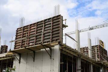 Reinforced concrete building under construction showing formwork scaffolding and steel rebar framework at an early stage of urban development against a partly cloudy sky