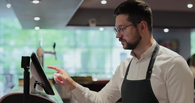 Bearded man waiter with glasses at counter with cash box working at bar or restaurant.