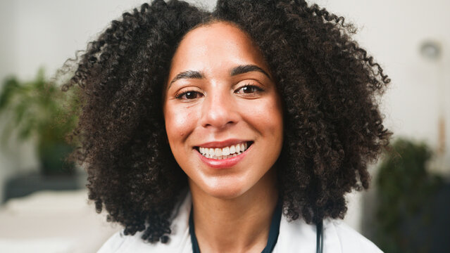 Smiling Woman With Curly Hair In Clinical Setting For Friendly Doctor Visit
