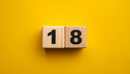 Wooden cubes with number 18 on smooth yellow background, top view.