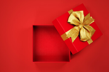 Open christmas gift box with golden bow open on red background top view. New year holiday present with gold ribbon mockup template.
