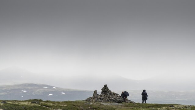 Two pilgrims lay stones at the stone pyramid Allmannr&oslash;ysa, cloudy landscape, pilgrimage route Olavsweg or Olavsleden, old Kongevegen or King's Path over the Dovrefjell, Norway