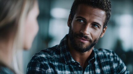 Fototapeta premium A man in a plaid shirt engages in a thoughtful conversation during a casual meeting in a softly lit indoor setting