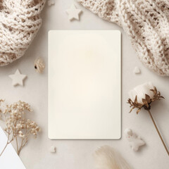 Blank card surrounded by cozy knitted fabric, dried flowers, and small decorative stars on soft background