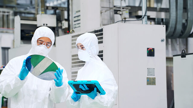 半導体工場でタブレットを持ってシリコンウエハーを検査する防護服を着た男女作業員