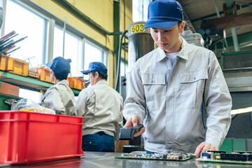 A male worker inspects products using a handheld terminal at a factory