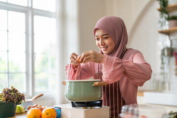 Muslim woman happy cooking healthy meal in kitchen wearing hijab making soup in pot with fresh vegetables food preparation activity nutrition, ramadan healthy recipe preparation, islamic food culture