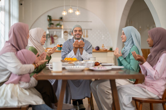 Muslim family praying before eating iftar meal during ramadan or eid together around dining table, tradition faith gratitude love, islamic culture peaceful moment with food and family, halal food