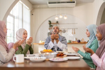 Muslim family praying before eating iftar meal during ramadan or eid together around dining table, tradition faith gratitude love, islamic culture peaceful moment with food and family, halal food