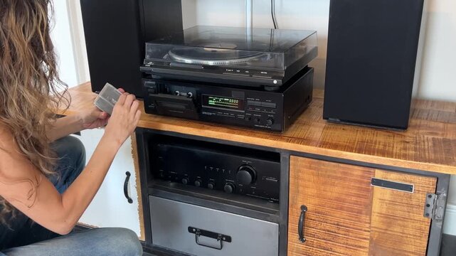 Plano medio de una mujer insertando una cinta de casete en una casetera vintage y poni&eacute;ndola a reproducir, 4K
