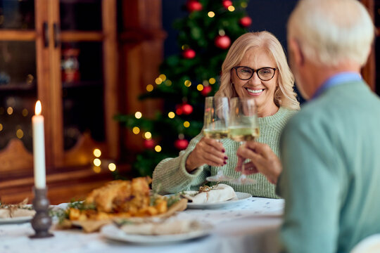 Couple Toasting Wine Glasses At Cozy Christmas Dinner With Tree And Candles - Powered by Adobe