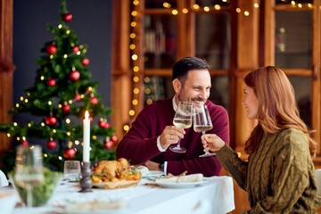 Couple Clinking Wine Glasses During Festive Christmas Dinner By Tree, Candlelight, and Home Holiday Meal