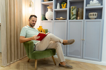 Man reading book relaxing in armchair at home