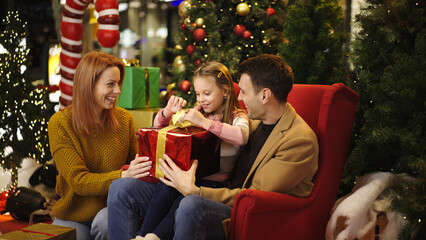 Family joyfully opens a Christmas gift together in a festive holiday setting
