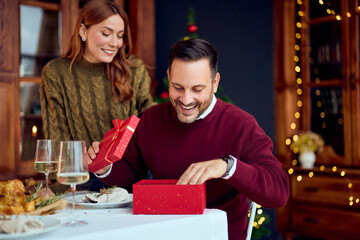 Joyful Couple Shares Holiday Gift At Festive Dinner Table During New Year Celebration