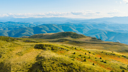 Fototapeta premium Bright aerial view of rolling green mountains and distant forest ridges