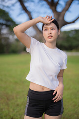 Young Asian woman wiping sweat from her forehead, taking a break outdoors on a sunny day after...