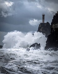 Powerful waves crash against a rocky shore with a lighthouse on a cliff