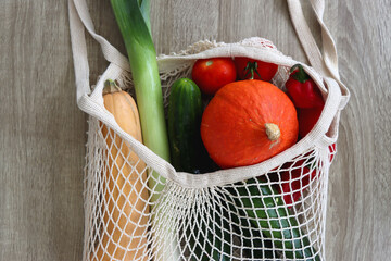 Mesh bag with various healthy vegetables on wooden background.