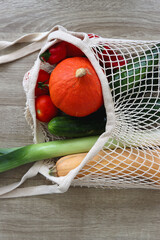 Mesh bag with various healthy vegetables on wooden background.